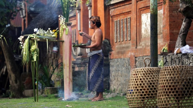 Tenganan, Indonesia - August 23, 2014: A man presents an offering for a traditional ceremony at the Tenganan Village, once one of the most secluded societies in Indonesia, it is now a tourist attraction due to its culture, architecture, and crafts. A visit is a step back in time.