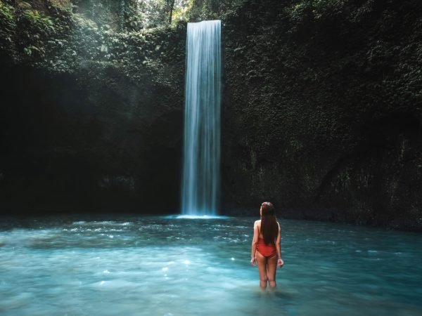 Traveling young woman with tropical rainforest in Bali enjoying life at beautiful Tibumana waterfall.