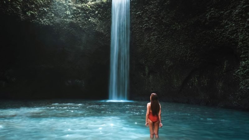 Traveling young woman with tropical rainforest in Bali enjoying life at beautiful Tibumana waterfall.