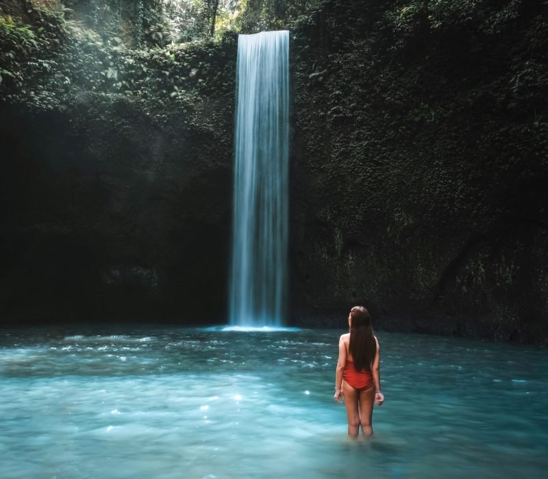 Traveling young woman with tropical rainforest in Bali enjoying life at beautiful Tibumana waterfall.